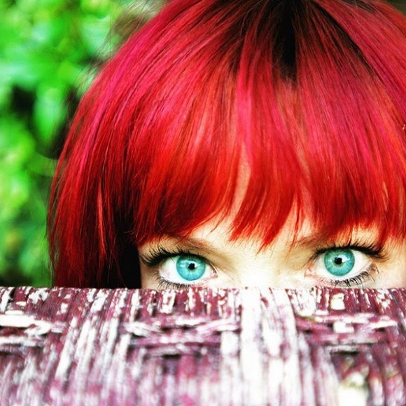 Candy Olsen, with bright red hair and green eyes, peeks over fence.