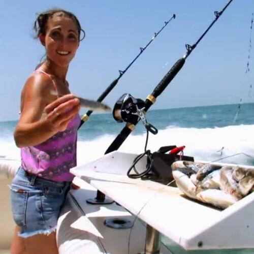 Mary Padian holds a small fish as she stands on a boat out in the ocean.