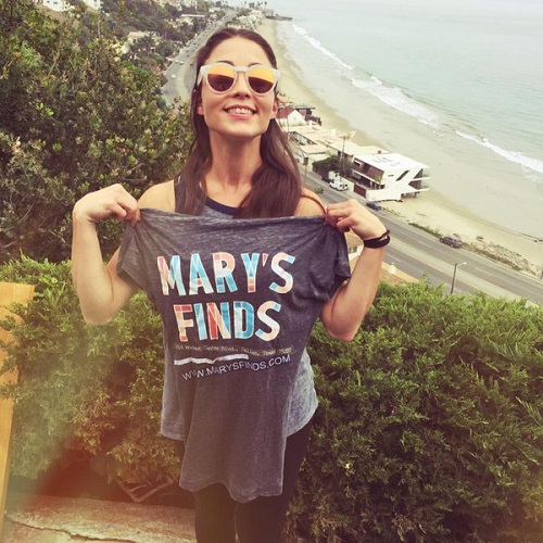 Mary Padian holds up t-shirt with ocean view in background